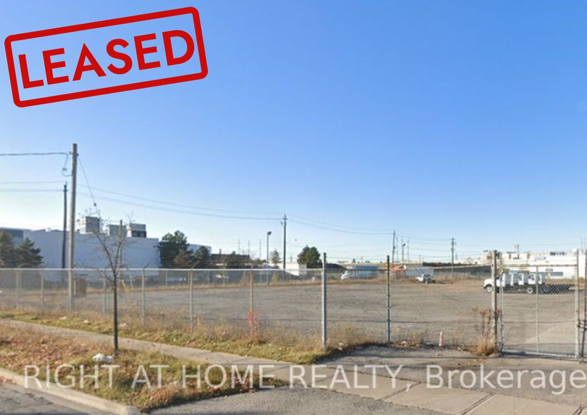 Empty fenced lot with clear blue sky and industrial buildings in background.