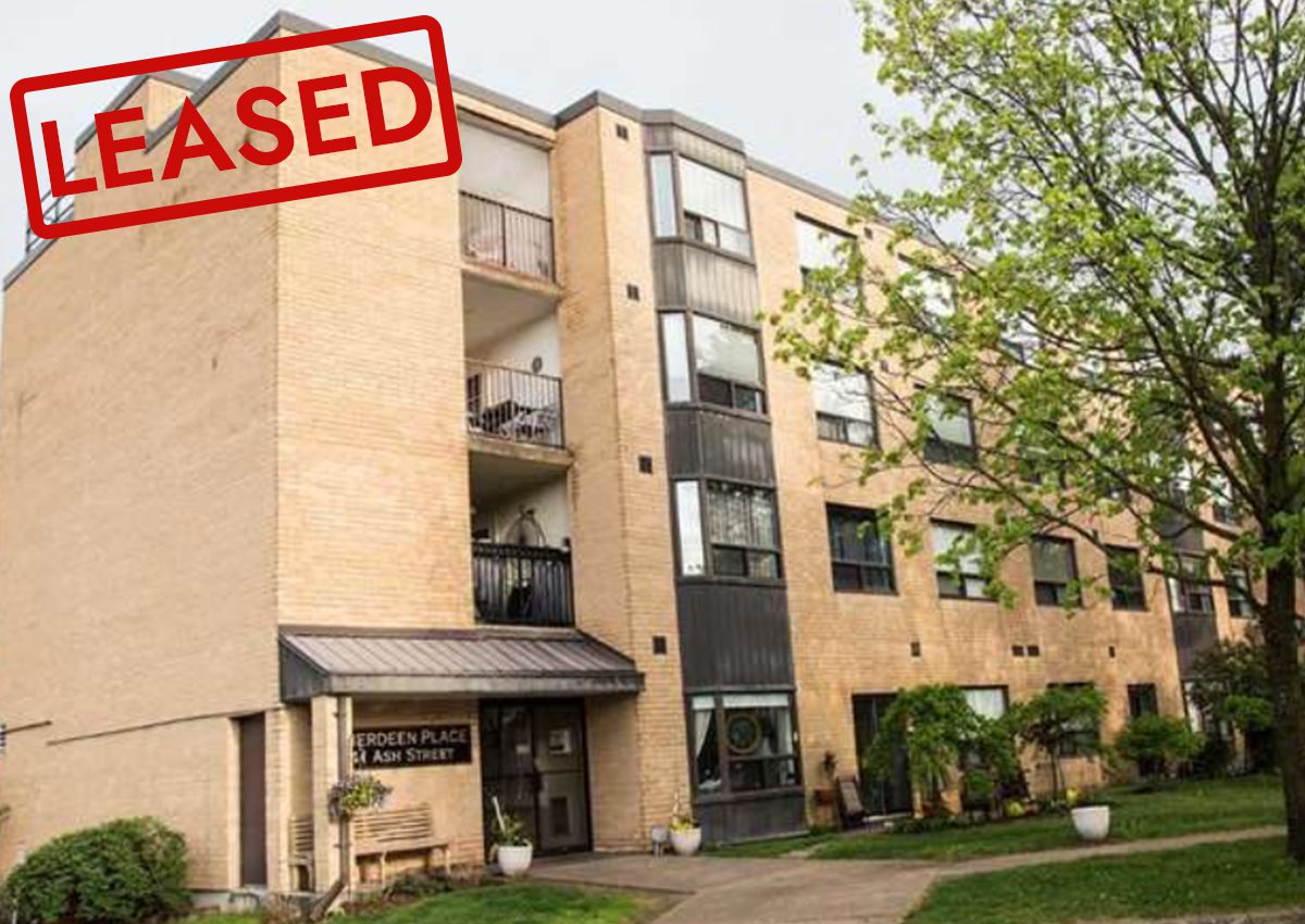 Exterior view of a residential apartment building with balconies and a large tree nearby.