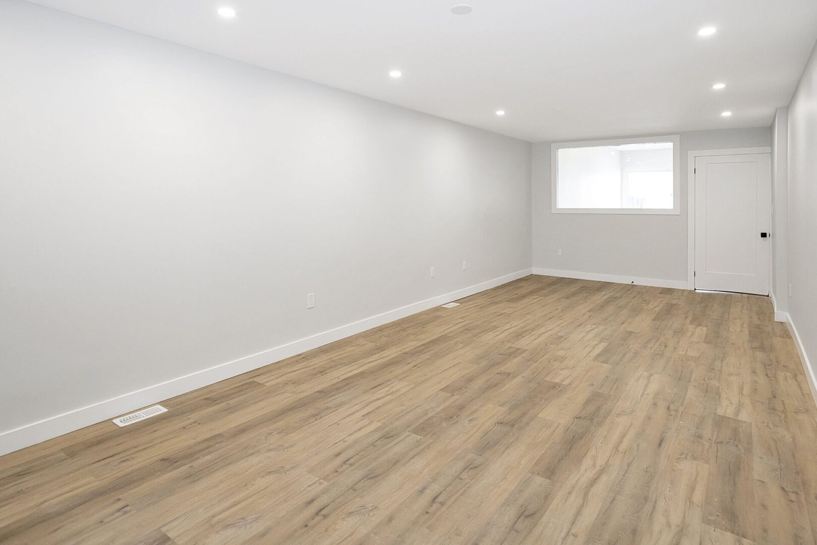 Empty room with wooden floor and white walls under recessed ceiling lights.