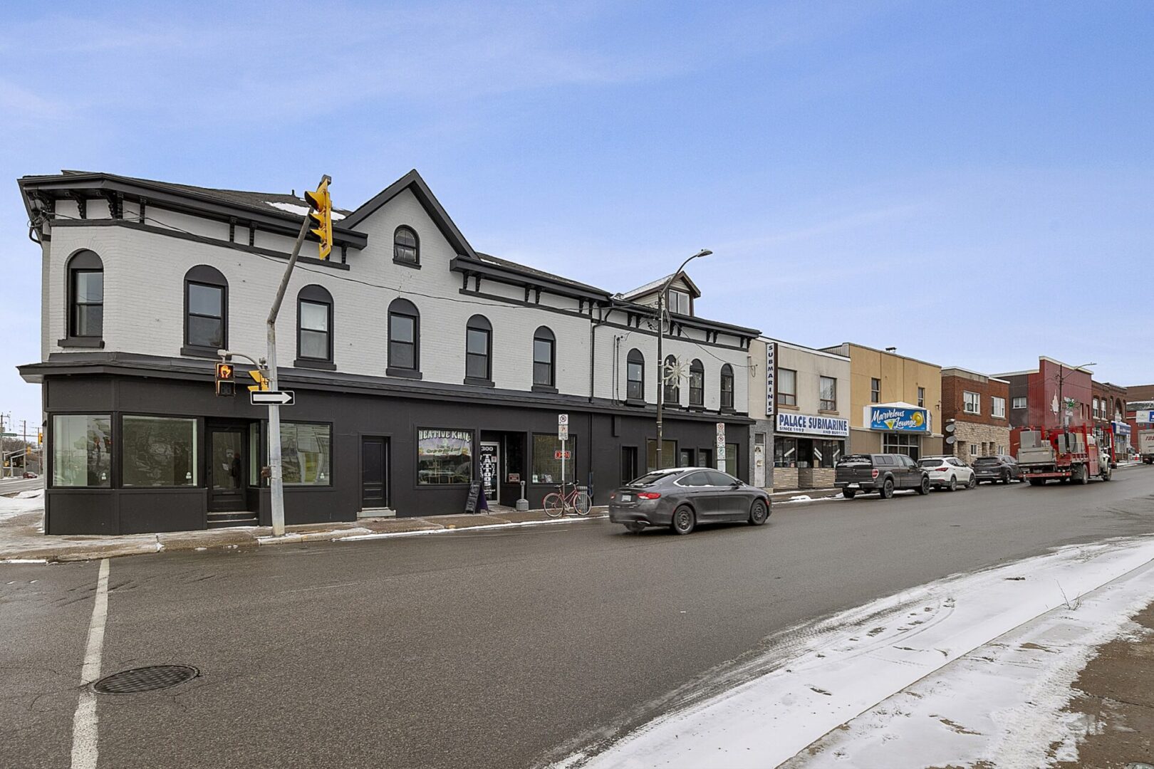 Historic buildings line a quiet street with parked cars and clear skies.
