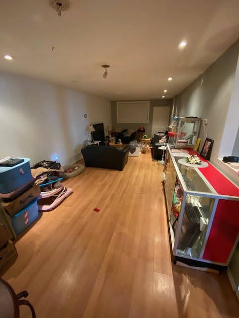 Living room with wooden floor and scattered furniture and items.