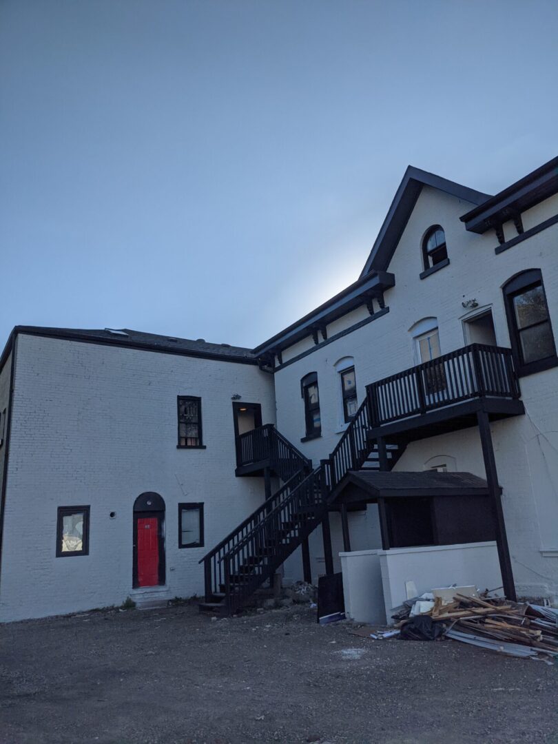 White multi-story building with outdoor black staircase and red door.