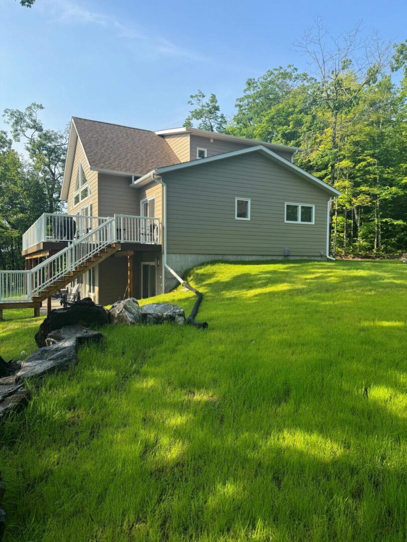 A house with a wooden deck surrounded by green grass and trees.