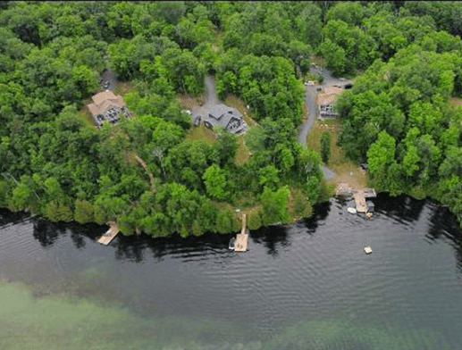 Aerial view of lakeside homes surrounded by dense forest and docks.