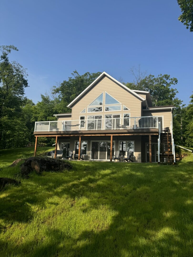 A spacious two-story house with large windows and a wooden deck surrounded by greenery.