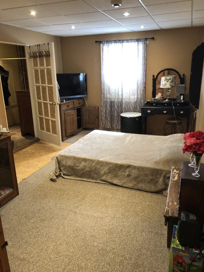 Cozy bedroom with beige tones, a bed, TV, and vintage furniture.