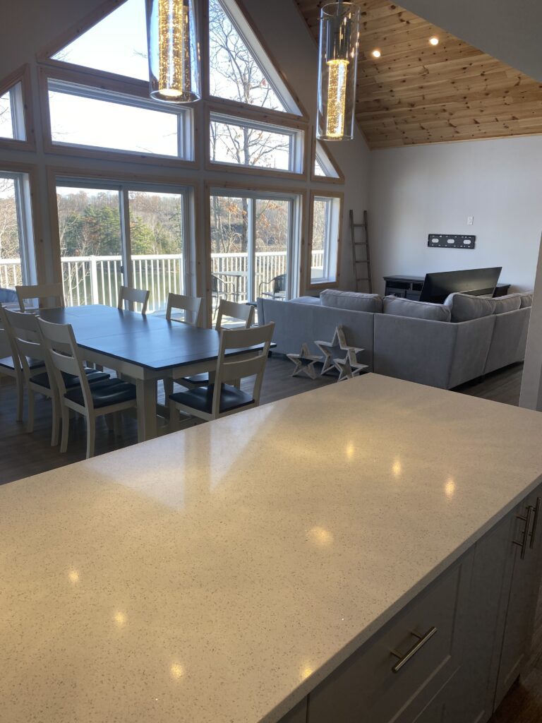 Bright dining and living area with large windows and wooden ceiling.